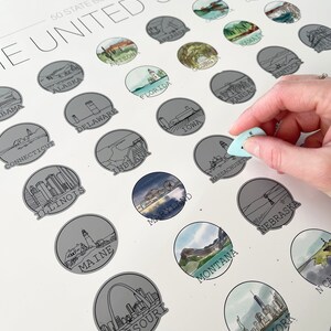 May include: A white 50 State Bucket List poster with illustrations of each state. The poster has a scratch-off design, with a hand holding a light blue scratch tool. The text "THE UNITED STATES" is at the top.