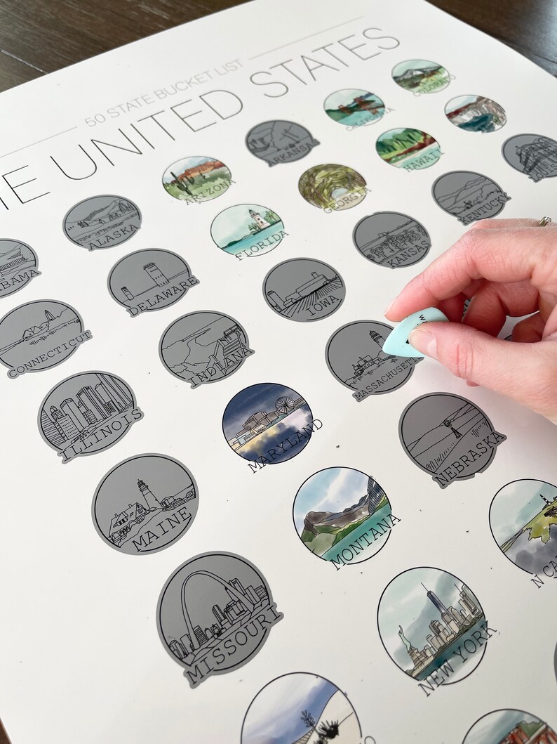 May include: A white 50 State Bucket List poster with illustrations of each state. The poster has a scratch-off design, with a hand holding a light blue scratch tool. The text "THE UNITED STATES" is at the top.