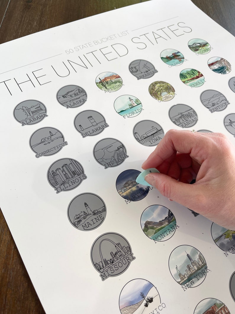 May include: A white poster titled "50 State Bucket List" featuring illustrated state icons. The poster is being scratched to reveal the state of Maryland. Each state icon is a unique watercolor illustration.