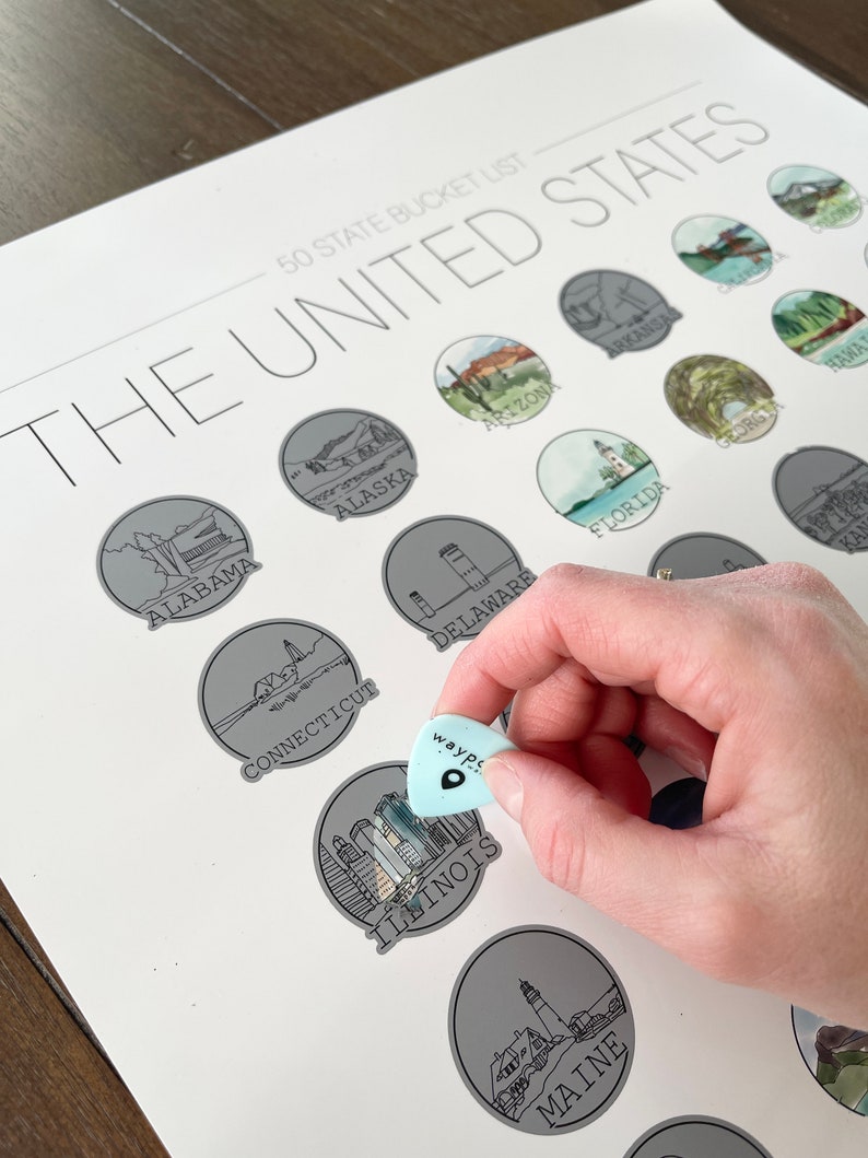 May include: A 50 State Bucket List print featuring illustrations of U.S. states. A light blue guitar pick with the word "wayp" is held over the Illinois illustration. The print includes state names and illustrations in a circular design.