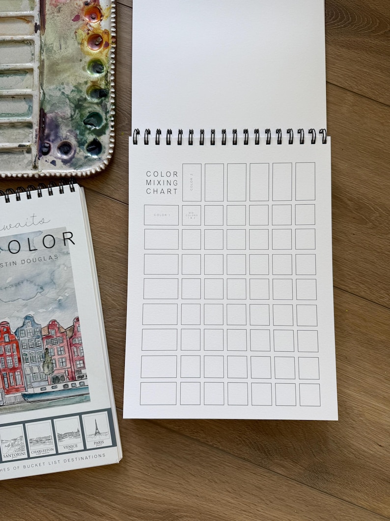 May include: A watercolor artist's setup featuring a spiral-bound color mixing chart, a watercolor palette with various paint colors, and a sketchbook titled "Color" with destination illustrations. The chart is open, ready for use.