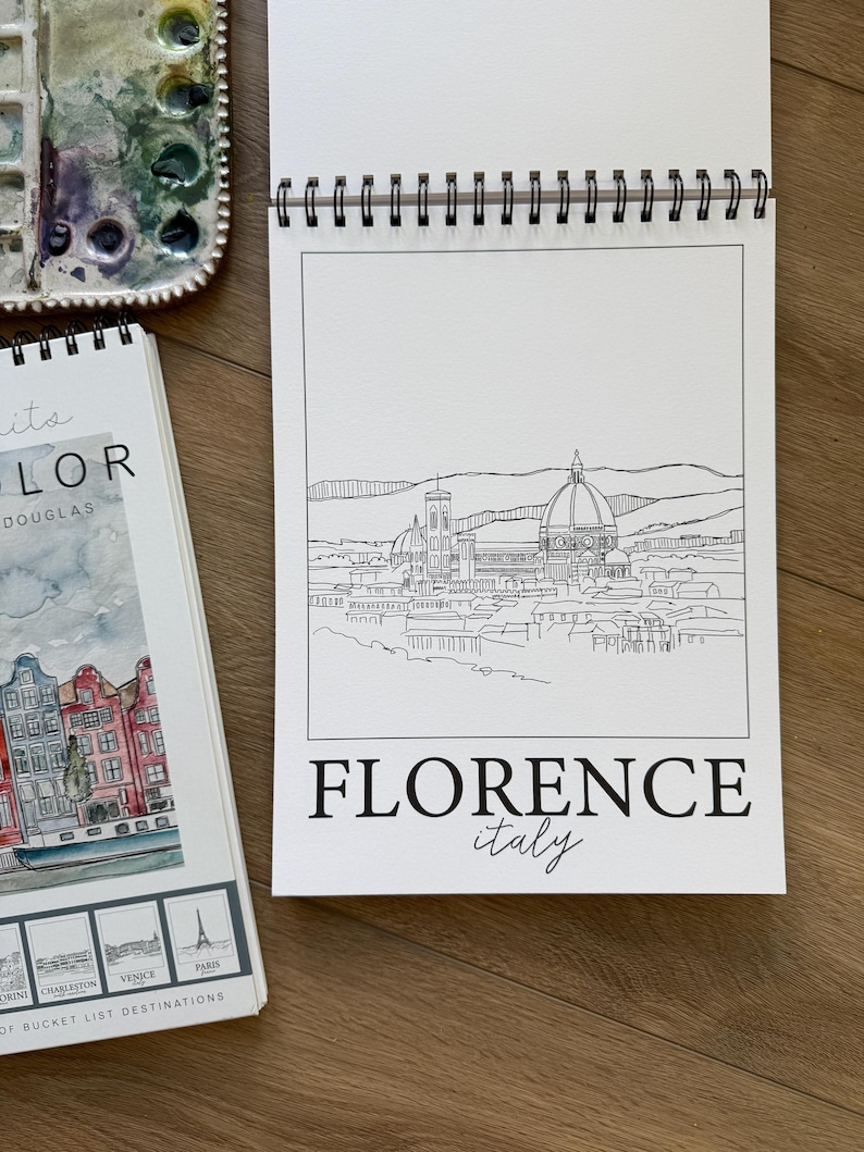 May include: A spiral-bound sketchbook featuring a black and white line drawing of Florence, Italy, with the text "FLORENCE italy" at the bottom. A watercolor palette and a travel-themed sketchbook are also visible.