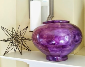 May include: A large, round, purple wooden urn with a smooth, polished finish. The urn is sitting on a white shelf.