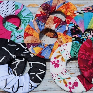 May include: Six colorful fabric ring holders with different patterns, including polka dots, floral, and abstract designs. The rings are made of fabric and are folded in a circular shape.