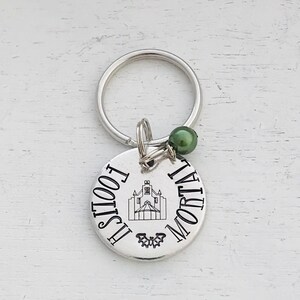 May include: Silver keychain with a round charm that says "This Fool is Mortal" with a small image of a haunted house and a bat. The charm has a green bead attached to the top.