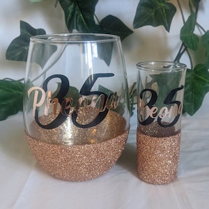 May include: Two gold glitter glasses with black vinyl lettering. The larger glass says "35 Pheona" and the smaller glass says "35 Pheona".