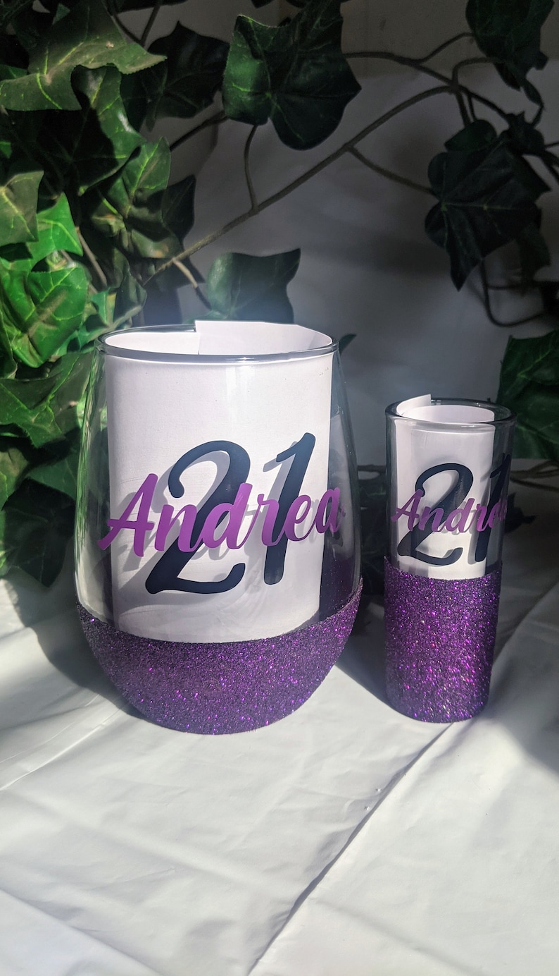 May include: Two purple glitter glasses with the number 21 and the name Andrea on them.