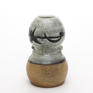 May include: A small, gray and brown ceramic vase with a black abstract design. The vase has a rounded body and a narrow neck.