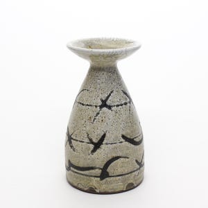 May include: A small, white ceramic vase with a flared top and a black and white abstract design. The vase has a speckled glaze and a slightly textured surface.