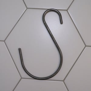 May include: A silver metal S-shaped hook. The hook is hanging on a white tiled wall.