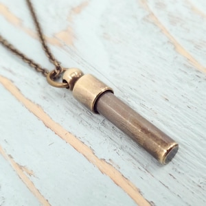Open brass urn necklace showing its threaded compartment for ashes or keepsakes, set on a light blue wooden background.