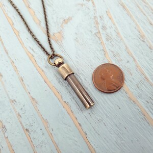 May include: A brass necklace with a cylindrical pendant that is about the size of a penny. The pendant has a cap on one end and is open on the other end.