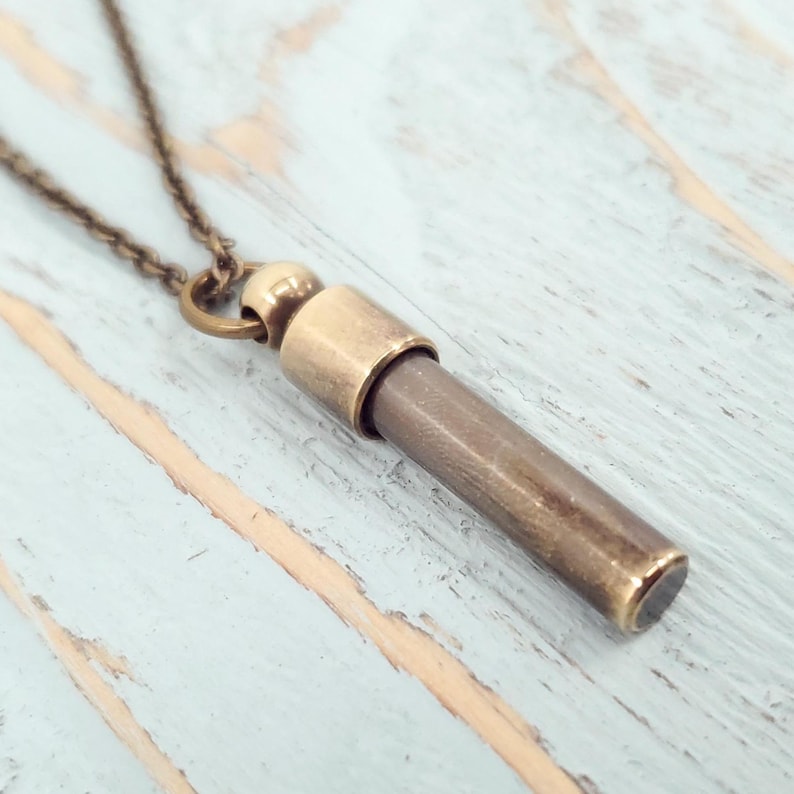 Open brass urn necklace showing its threaded compartment for ashes or keepsakes, set on a light blue wooden background.