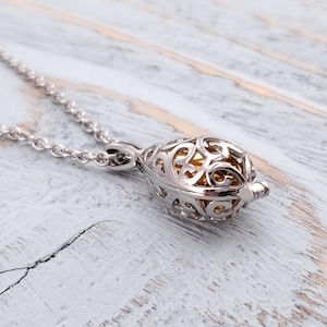May include: Silver chain necklace with a silver and gold filigree pendant. The pendant is shaped like a teardrop and has a small opening at the top.