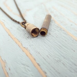 May include: A brass necklace with a small, cylindrical pendant that opens to reveal a hollow interior. The pendant is attached to a delicate chain.