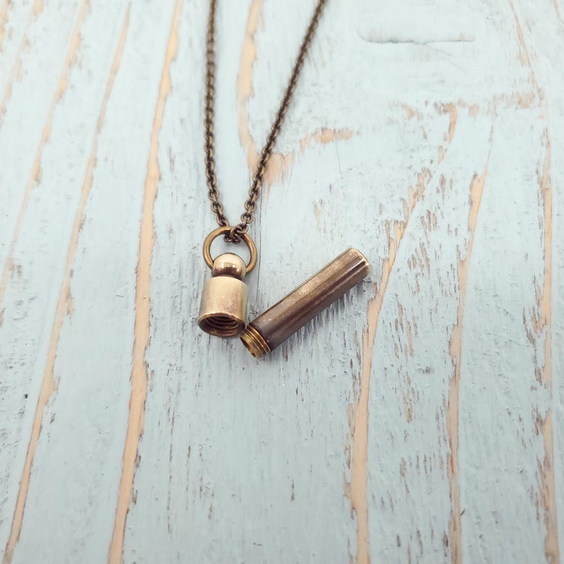 May include: A brass necklace with a small, cylindrical pendant that opens to reveal a hollow interior. The pendant is attached to a delicate chain.