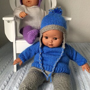 May include: Two knitted doll outfits, one in blue and gray and one in white and purple. Both outfits include a hat, sweater, and pants.