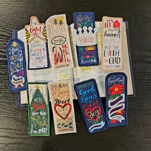 May include: A set of 10 colorful embroidered bookmarks with religious and inspirational quotes. The bookmarks feature a variety of designs, including a Christmas tree, a heart, a crown, and a flower. The quotes include "The light shines in the darkness", "Joy to the world", "He is the Prince of Peace", "Let the heavens rejoice", "A merry heart does good like medicine", "Bring you good news of great joy", and "Emmanuel".