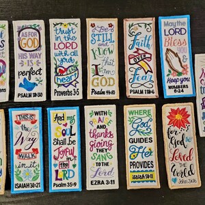 May include: A collection of 12 colorful embroidered bookmarks with bible verses and scripture references. The bookmarks are rectangular and feature a variety of floral and heart designs.
