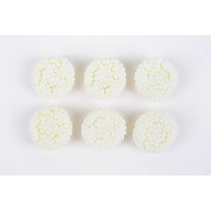 Könnte beinhalten: Sechs weiße Bonbons mit strukturierter Oberfläche, die kleinen Perlen ähneln. Die Bonbons sind in zwei Reihen zu je drei auf weißem Hintergrund angeordnet.