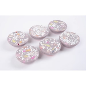 May include: Six round, gray coasters with a speckled, terrazzo-like design. The coasters have a white base with colorful flecks throughout.