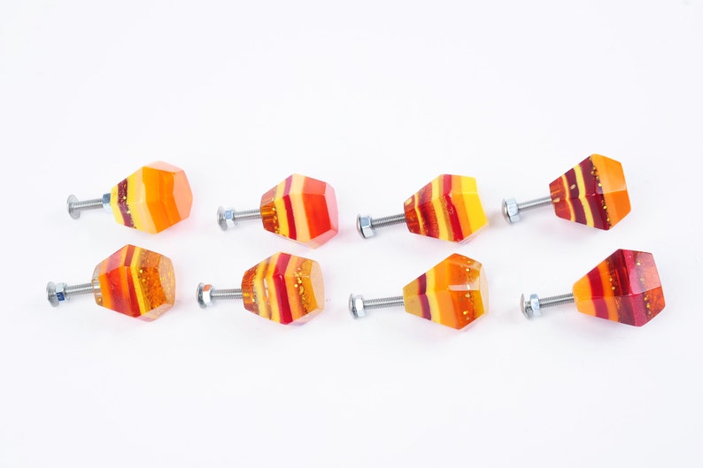 Op de afbeelding: Acht kleurrijke glazen kastknoppen met een gelaagd ontwerp in tinten rood, oranje en geel. Elke knop heeft een zilveren schroef.