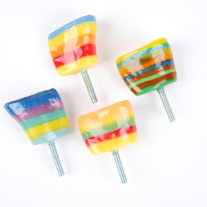 Op de afbeelding: Vier kleurrijke regenboogkleurige kastknoppen met zilveren schroeven. De knoppen zijn gemaakt van hars en hebben een glanzende afwerking.