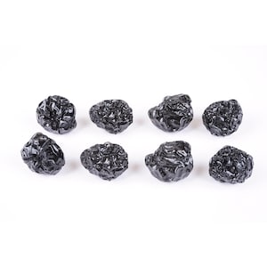 Op de afbeelding: Acht zwarte gedroogde pruimen, ook wel pruimen genoemd, zijn gerangschikt in twee rijen van vier op een witte achtergrond.