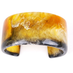 Könnte beinhalten: Ein breites, gelbes und schwarzes Resin-Armband mit Marmorierung.