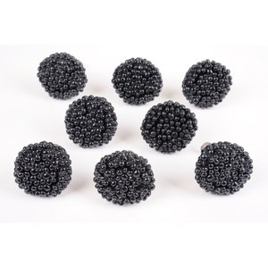 May include: Eight black round cabinet knobs with a textured surface. The knobs are made of a material that resembles small black beads.