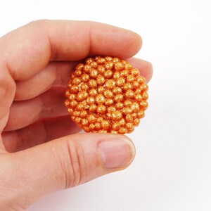 May include: A round, orange, glittery ornament made of small, round beads.