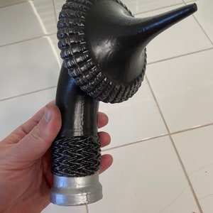 May include: A black, ornate, decorative walking stick handle with a silver base. The handle is shaped like a curved horn with a textured, woven design.