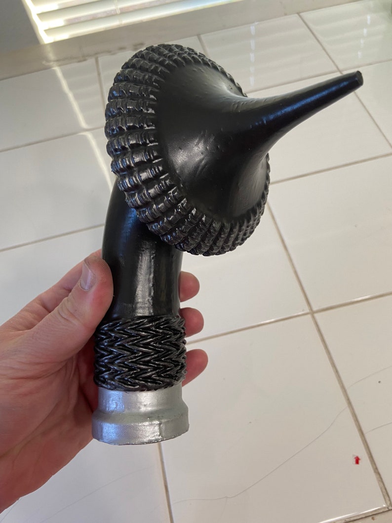 May include: A black, ornate, decorative walking stick handle with a silver base. The handle is shaped like a curved horn with a textured, woven design.