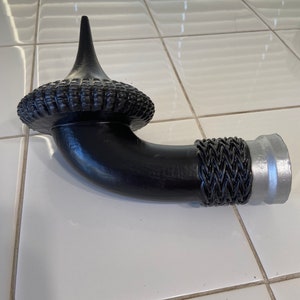 May include: A black metal pipe with a decorative woven design and a silver metal end cap. The pipe has a curved shape and a pointed top.