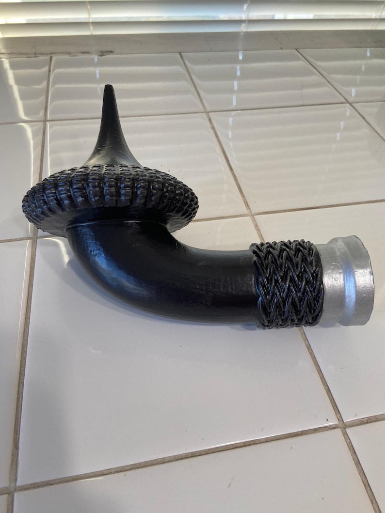 May include: A black metal pipe with a decorative woven design and a silver metal end cap. The pipe has a curved shape and a pointed top.