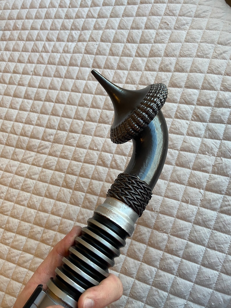 May include: A black lightsaber with a silver and black ribbed handle and a black, spiky, cone-shaped hilt.