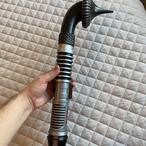 May include: A black and silver lightsaber with a curved handle and a black and silver hilt. The lightsaber has a red blade.