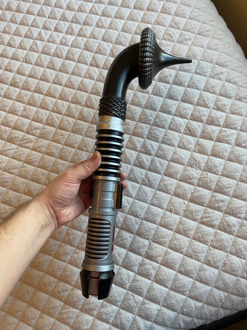 May include: A black and silver lightsaber with a curved handle and a black and silver hilt. The lightsaber has a red blade.