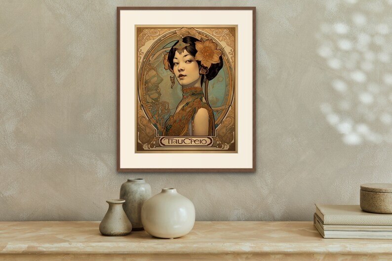 May include: A framed art print featuring a woman with dark hair and a floral headpiece. The woman is wearing a gold and brown patterned dress. The print is in an Art Nouveau style and includes the text "TrauCrejo".