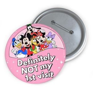 May include: A round pin-back button featuring a pink background with white sparkles and a group of cartoon characters including Mickey Mouse, Minnie Mouse, Donald Duck, Daisy Duck, Goofy, and Pluto. The text reads: Definitely NOT my 1st visit.