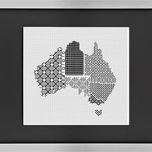 May include: Framed artwork depicting a cross-stitch style map of Australia. The map is segmented, each part filled with a different black and white geometric design. The artwork is presented on a white background, within a black mount and a silver frame.