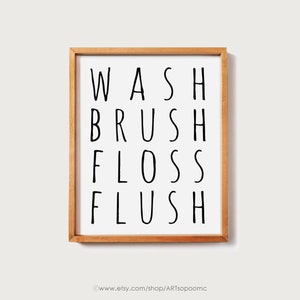 Peut inclure: Impression encadr&eacute;e avec les mots "WASH BRUSH FLOSS FLUSH" en noir, police sans-serif. L'impression est sur fond blanc et encadr&eacute;e dans un cadre en bois brun clair. L'adresse du site web est au bas du cadre.