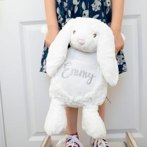 May include: A white plush bunny with long ears and a pink nose. The bunny has the name "Emmy" embroidered on its chest in silver glitter.