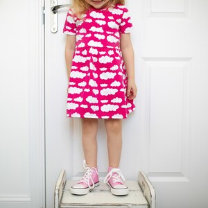 May include: A young girl wearing a pink dress with a white cloud print and pink high-top sneakers.