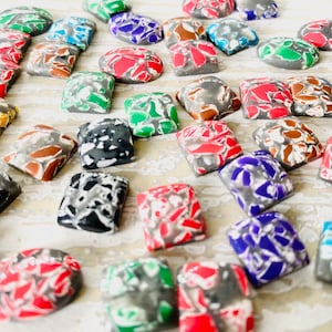 May include: A selection of mosaic-style polymer clay beads in various shapes and colours. The beads feature red, green, blue, grey, and white. Some are square, others are oval, and all have a textured, broken-stone appearance.