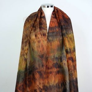 Può includere: Una sciarpa di seta trasparente con un motivo tie-dye in tonalità di marrone, arancione e verde. La sciarpa è drappeggiata su un manichino.