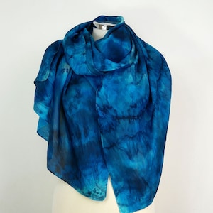 Op de afbeelding: Een blauwe zijden sjaal met een tie-dye patroon. De sjaal is gedrapeerd over een wit mannequin.