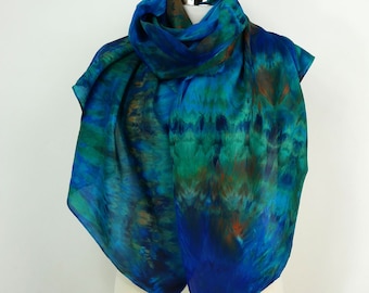 May include: A blue, green and brown silk scarf with a tie-dye pattern. The scarf is draped over a white mannequin.