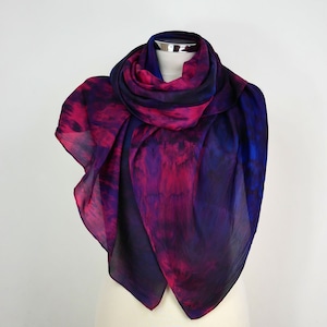 May include: A purple and pink silk scarf with a tie-dye pattern. The scarf is draped over a white mannequin.