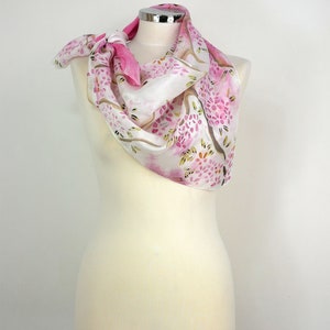 May include: A white silk scarf with a pink floral pattern. The scarf is tied around a white mannequin's neck.